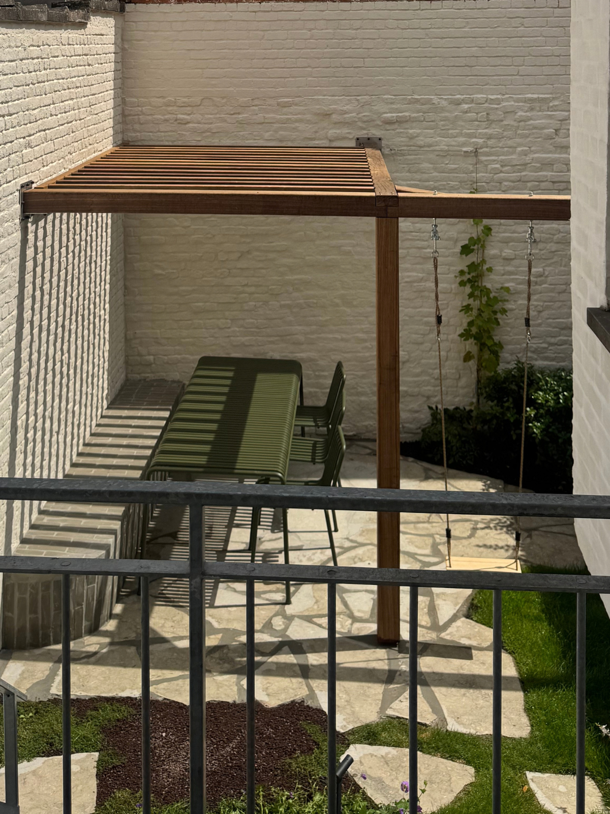 Houten terrasoverkapping op maat met groene tuintafel en schommel in een binnenhof