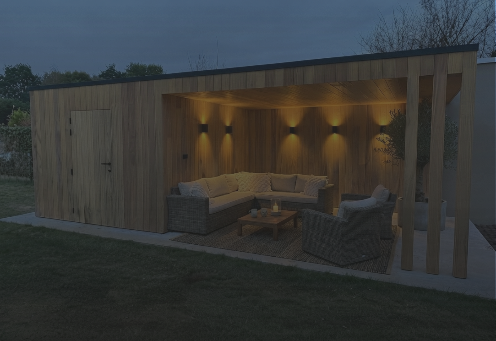 Houten bijgebouw op maat met verlichte leefruimte in een tuin bij avond